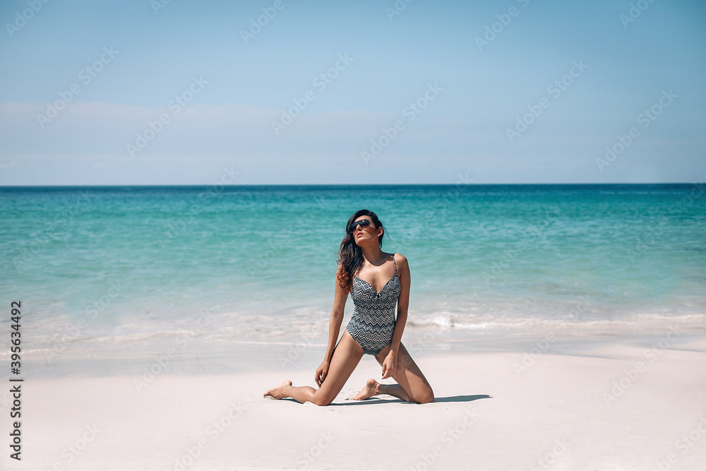 Beautiful girl with long wet hair posing on beach near ocean. Indian woman in bathing suit sitting on shore. Concept of travel. Phuket. Thailand