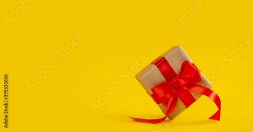 Gift box in craft paper with red ribbon bow on yellow color backdrop.