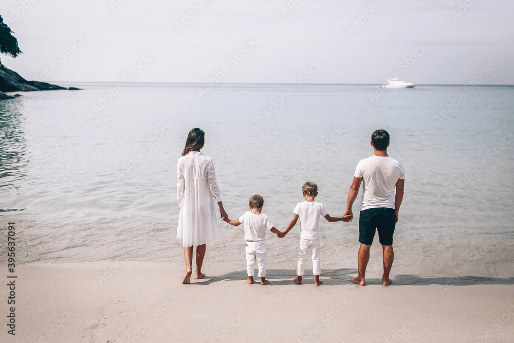 Happy young family in white clothes watching the sunset at the beach. Happy Family Lifestyle. On the background of a yacht away. Vacation. Phuket. Thailand Happy young family in white clothes watching the sunset at the beach. Happy Family Lifestyle. On the background of a yacht away. Vacation. Phuket. Thailand