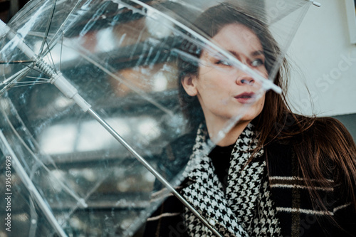 Outdoor portrait of stylish woman walking in park with transparent umbrella wearing trendy blue coat. Autumn fashion