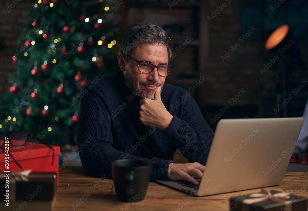 handsome man using laptop, shopping online. Christmas tree in the background. handsome man using laptop, shopping online. Christmas tree in the background.