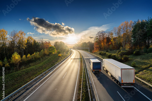 Obraz na płótnie Fast delivery van overtaking white truck on the asphalt highway in autumn forested landscape at sunset w salonie
