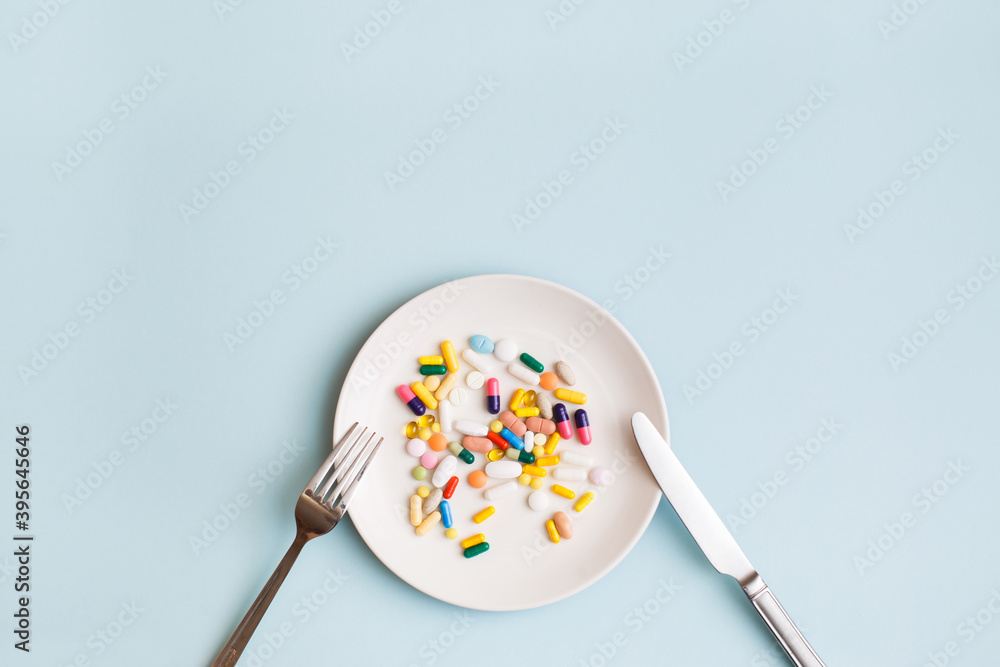 Creative medical layout made with colorful pills, capsules and supplements on white plate on light blue background. Minimal modern pharmacy or health care concept. Flat lay, top view, copy space Creative medical layout made with colorful pills, capsules and supplements on white plate on light blue background. Minimal modern pharmacy or health care concept. Flat lay, top view, copy space
