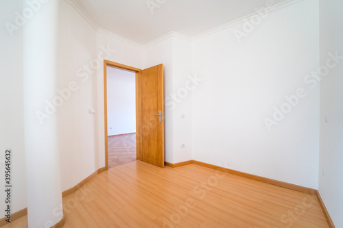 Empty room with wooden floating laminate flooring and door. House interior, wide bedroom space. Newly recently painted new apartment or house. Wood floor. Real state and property management
