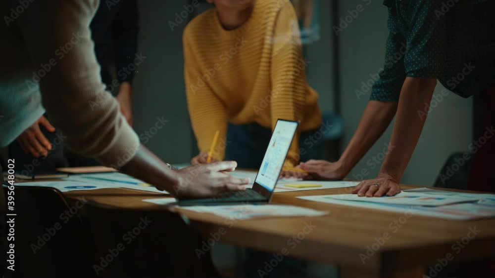 Close Up of Diverse Multiethnic Team Having Conversation in Meeting Room in a Creative Office. Colleagues Lean On a Conference Table, Look at Laptop Computer and Make Notes with Pencils on Notebooks. Close Up of Diverse Multiethnic Team Having Conversation in Meeting Room in a Creative Office. Colleagues Lean On a Conference Table, Look at Laptop Computer and Make Notes with Pencils on Notebooks.