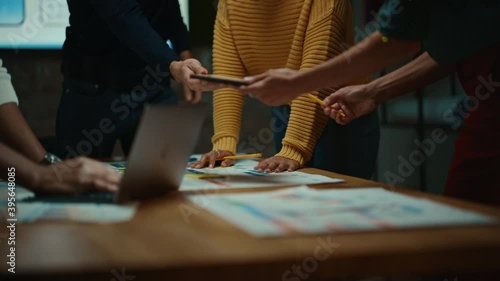 Close Up of Diverse Multiethnic Team Having Conversation in Meeting Room in a Creative Office. Colleagues Lean On a Conference Table, Look at Laptop Computer and Make Notes with Pencils on Notebooks.