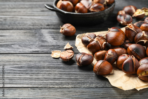 Tasty roasted edible chestnuts on black wooden table, closeup. Space for text