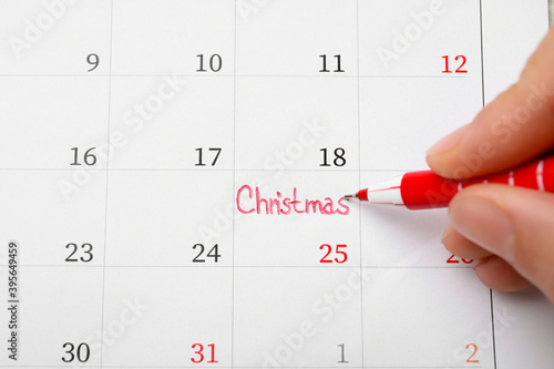 Woman writing word Christmas on calendar  top view. Holiday countdown