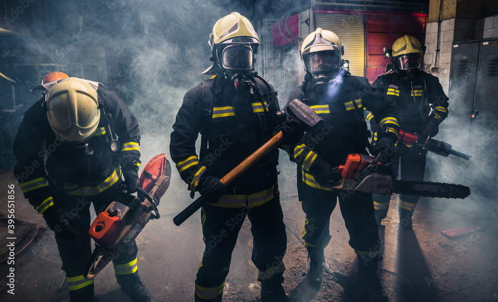 Group of firefighters with chainsaw and sledge hammer practicing in the garage of the fire department Group of firefighters with chainsaw and sledge hammer practicing in the garage of the fire department
