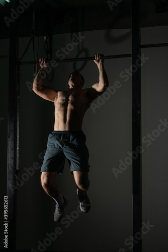 Handsome bodybuilder doing pull-ups on horizontal bar in a indoors modern gym. © qunica.com