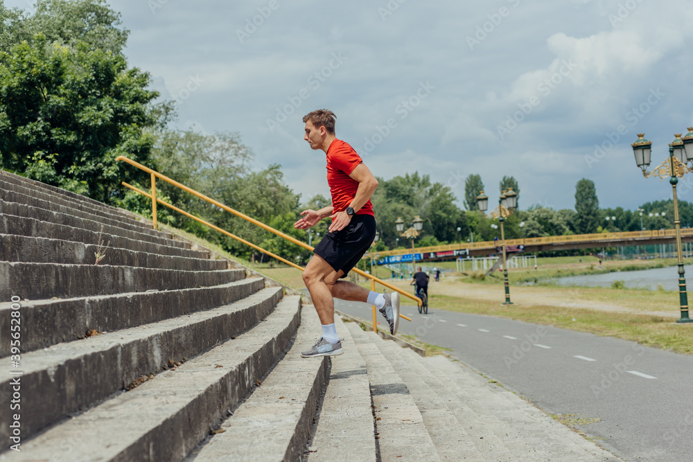 Young attractive male athlete exercising and running up on the stairs in the park.