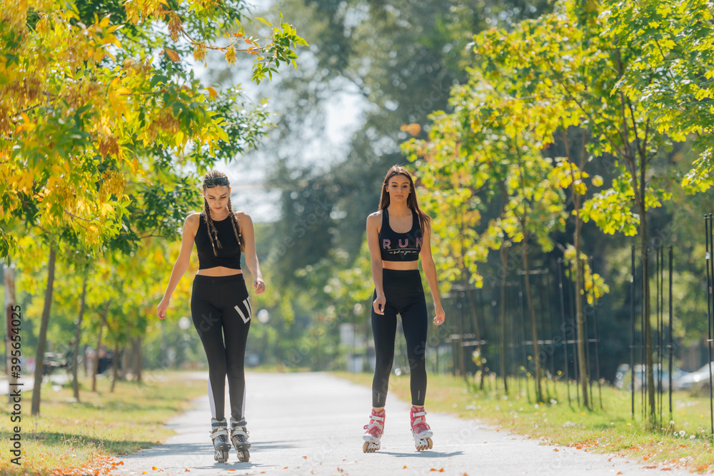 Obraz premium Full body portrait of happy sportswomen rollerskating in the park on a sunny day