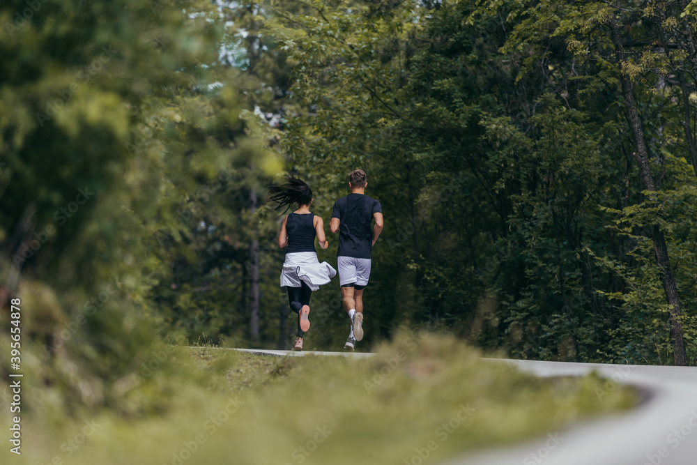 Young fit couple atheltes running on running road in a forest.