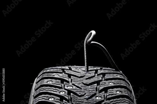 huge nail on a tyre over black background. studio shot. copy space. repair car tire concept. trouble on path conceptual