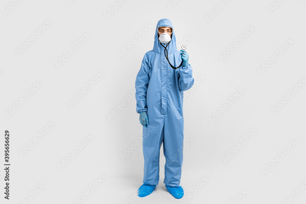 Doctor in a protective suit against coronavirus, mask, glasses and gloves is holding a stethoscope, listening to something, Medicine and healthcare concept Doctor in a protective suit against coronavirus, mask, glasses and gloves is holding a stethoscope, listening to something, Medicine and healthcare concept
