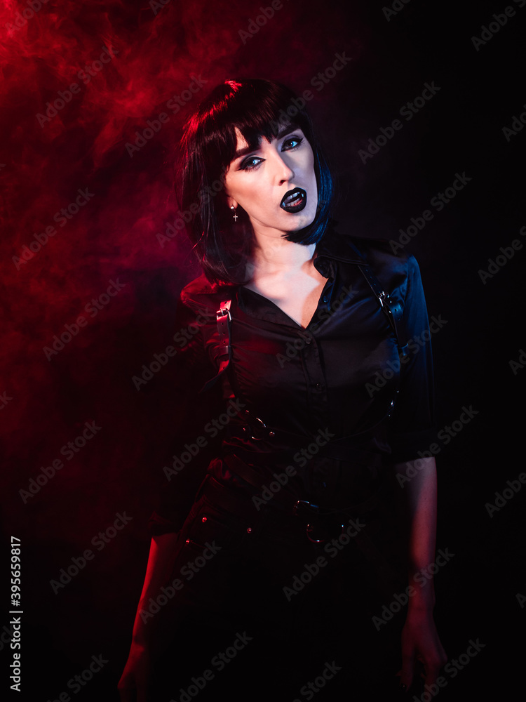 Girl on a black background with red and blue light in the form of a vampire. She demonstrates her wings and stares sharply into the camera.