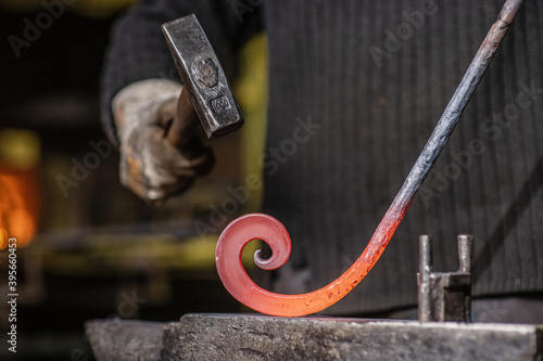 A blacksmith forging a curl from a red-hot flattened billet with a hammer. Handmade in the forge concept photo