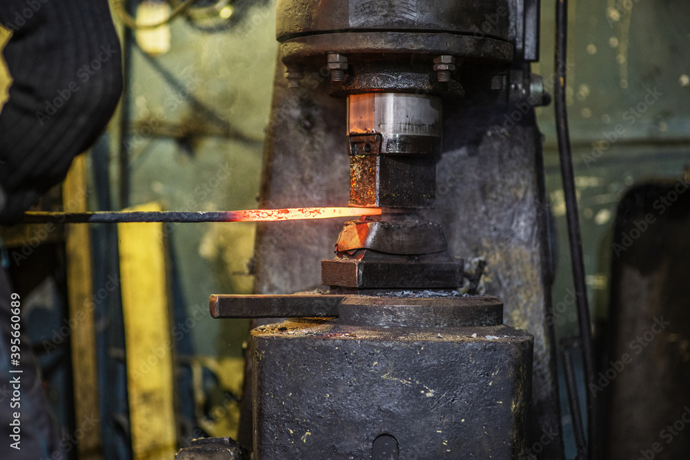 A blacksmith forges an iron rod with a mechanical hammer. Work in the forge A blacksmith forges an iron rod with a mechanical hammer. Work in the forge