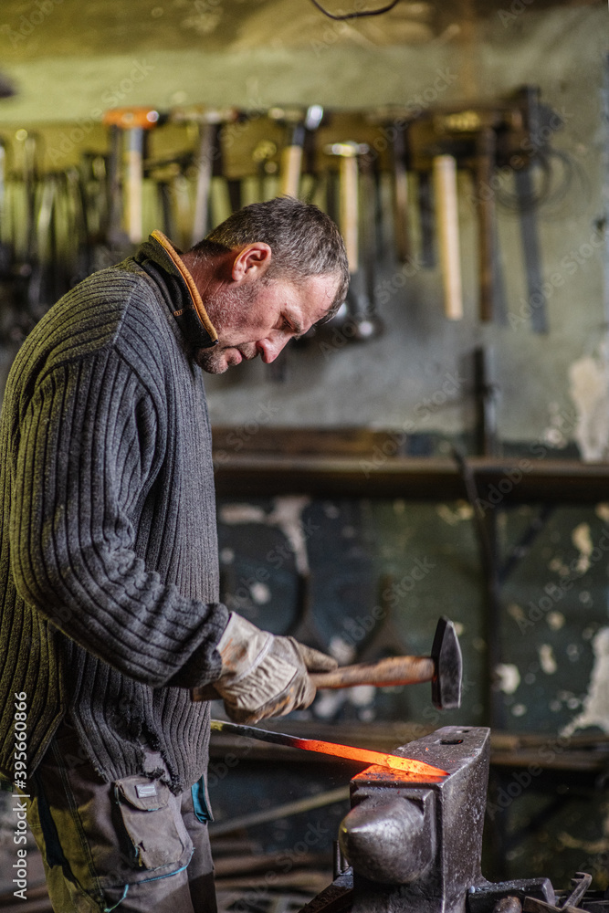 A blacksmith forging a red-hot iron billet on an anvil with a hammer. Handicraft concept A blacksmith forging a red-hot iron billet on an anvil with a hammer. Handicraft concept