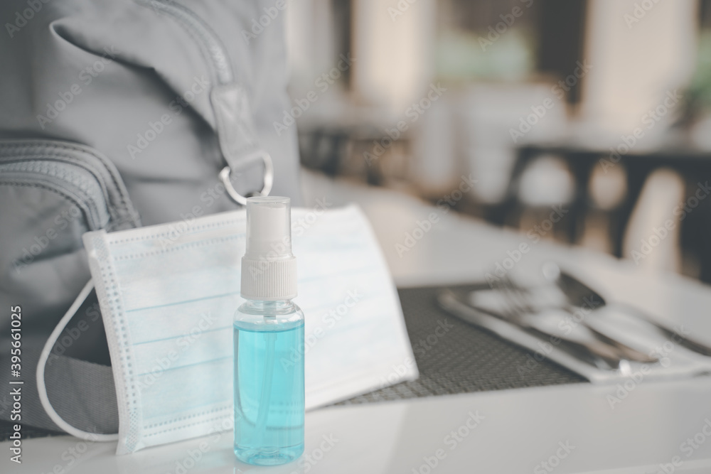 blue alcohol spray bottle with blurred surgical mask and lady's bag in restaurant ,new normal lifestyle concept
