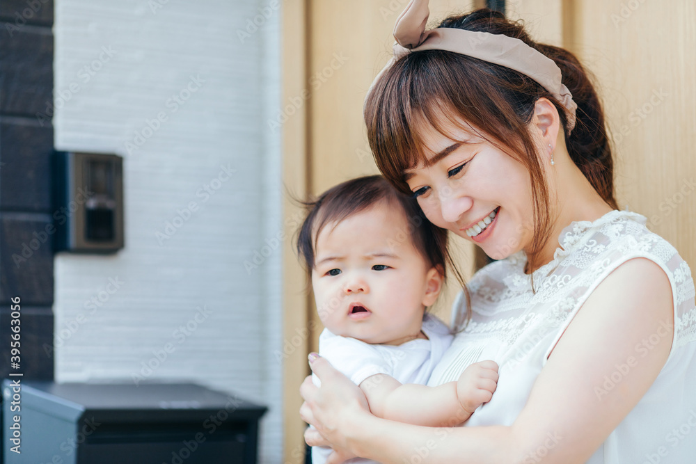 マイホームの前で赤ちゃんを抱く若い女性
