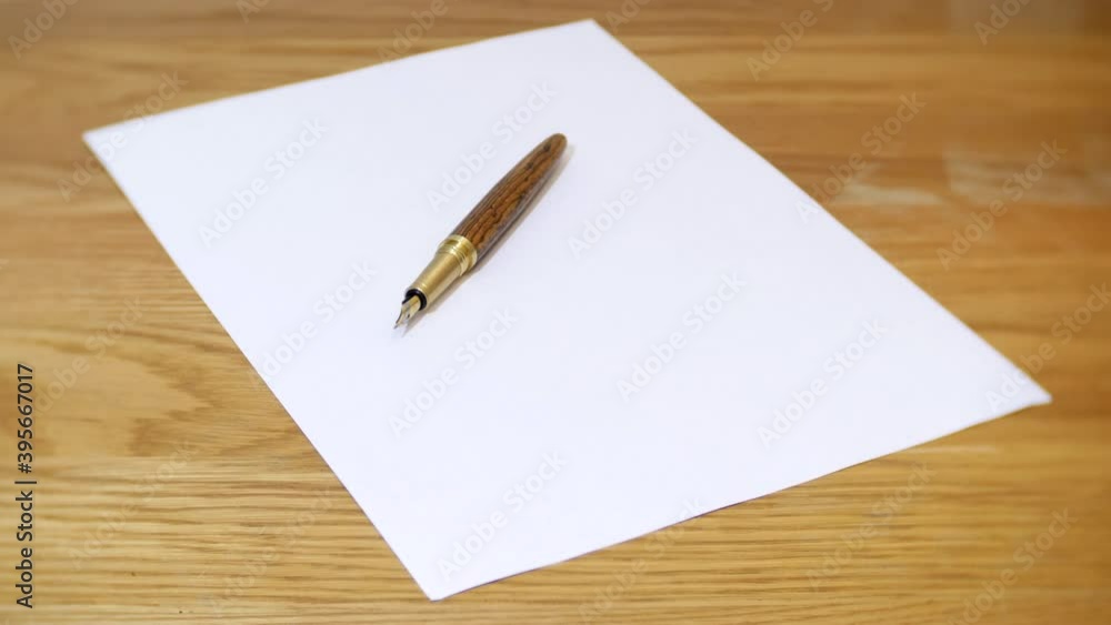 A sheet of blank white paper is placed on a wooden desk. A fountain pen is placed on top of the paper. A sheet of blank white paper is placed on a wooden desk. A fountain pen is placed on top of the paper.
