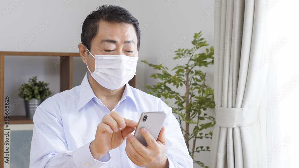 マスクをつけてスマホを操作する中高年の男性 マスクをつけてスマホを操作する中高年の男性