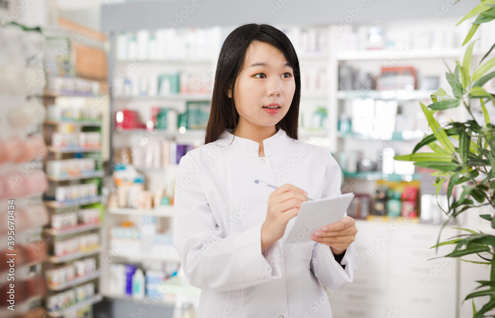 Chinese female is checking medicine with notebook in pharmacy. High quality photo