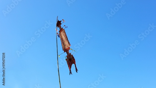 Tung or red flag on a bamboo pole. Made from local woven cloth as an ornament in various merit-making events of Thailand. On a beautiful blue background with a copy space. Selective focus 