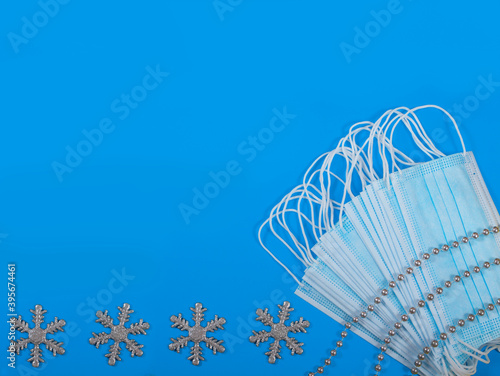 Blue protection masks with sterling silver beads on them and snowflakes on blue backround. Coronavirus protection. Christmas and Bew year concept. Flat lay. Copy space