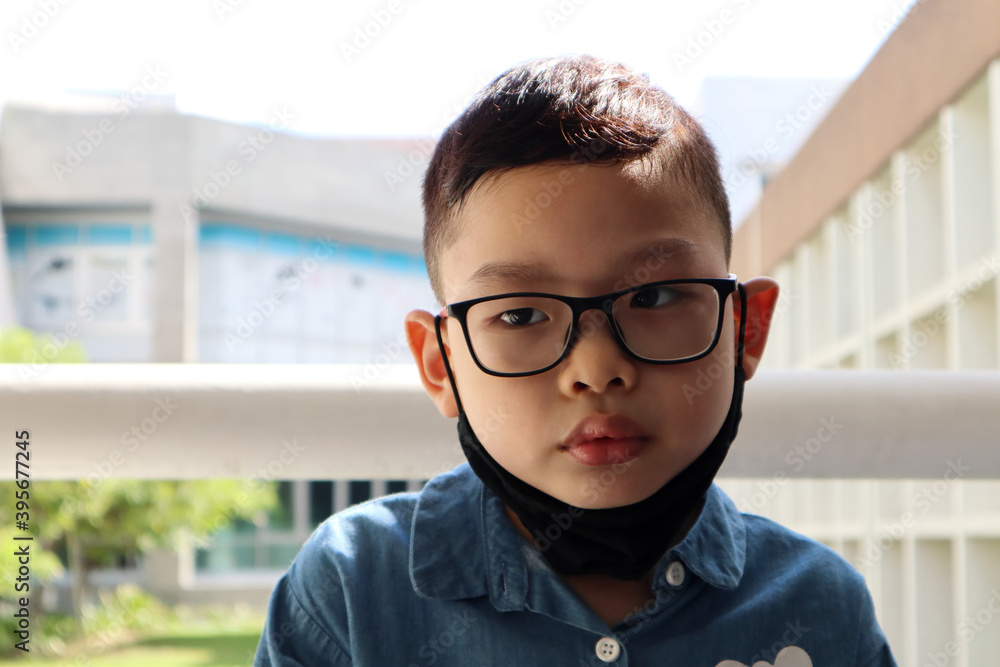 a portrait photo of asian young short hair boy kid wearing glasses , black  cloth mask and