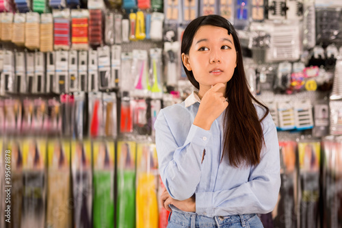 Portrait of cheerful positive glad Asian girl having doubts about choice of goods in cosmetics store