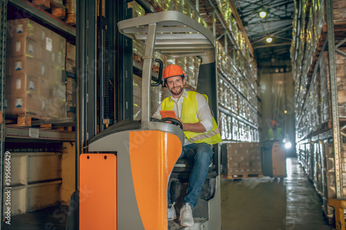 Young bearded worker sitting at the loader watching something on the tablet