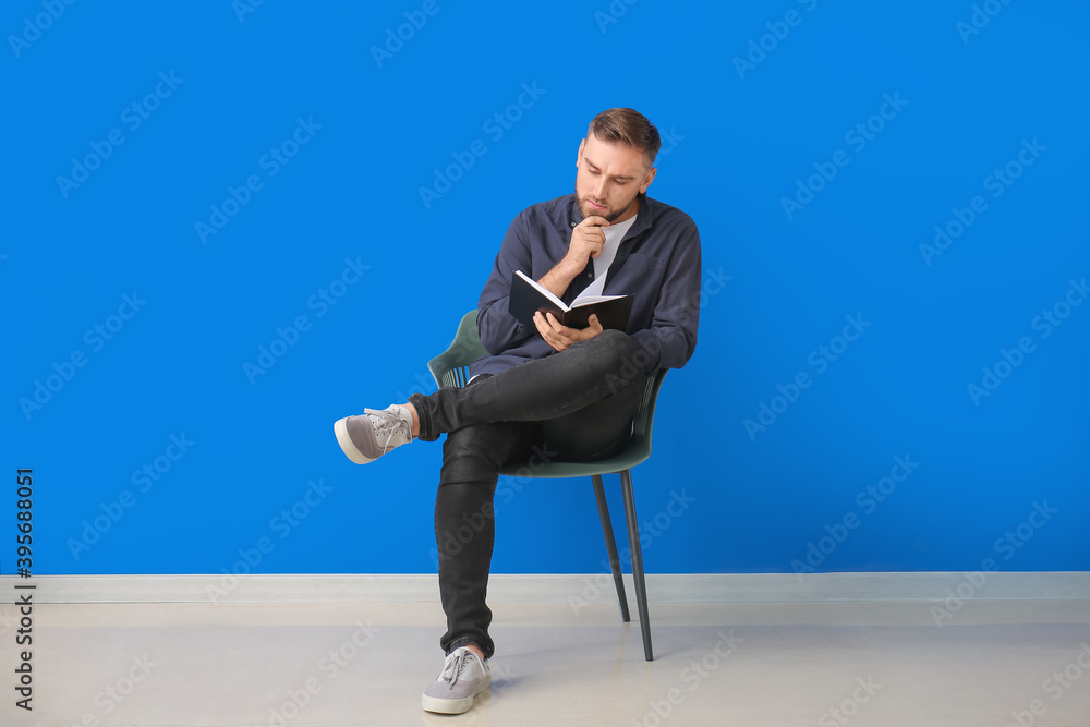 Young man reading book while sitting in armchair near color wall Young man reading book while sitting in armchair near color wall
