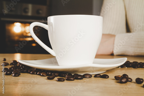 Small cup of hot coffee and fresh unground coffee beans scattered on a wooden kitchen table.