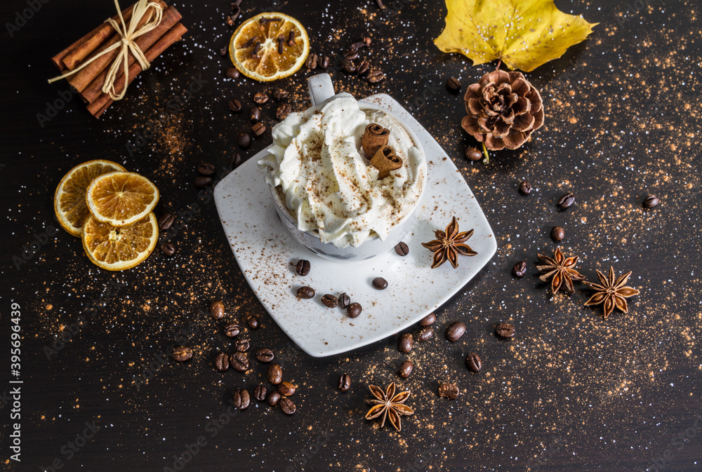 Fototapeta premium Cup of coffee with cinnamon sticks, whipped cream, chocolate sprinkles and star anise. Cozy winter or autumn hot beverage composition.