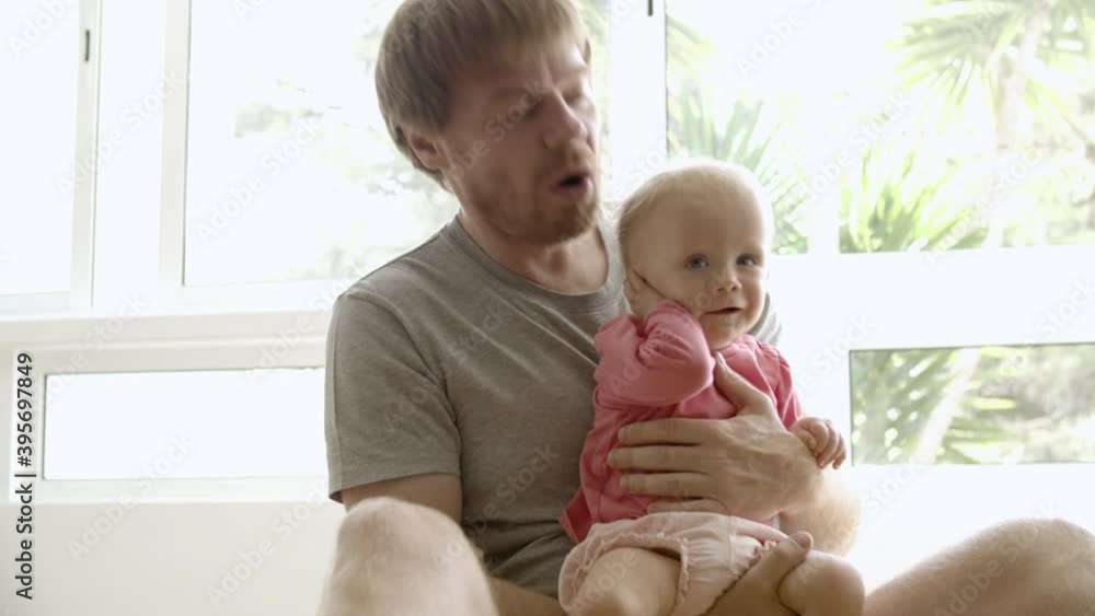 Happy father holding baby on hands, playing, talking with girl and sitting on floor indoors. Cheerful Caucasian dad having fun with funny infant. Being at home. Fatherhood and family time concept Happy father holding baby on hands, playing, talking with girl and sitting on floor indoors. Cheerful Caucasian dad having fun with funny infant. Being at home. Fatherhood and family time concept