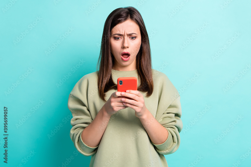 Photo portrait of unhappy astonished woman holding phone in two hands isolated on vivid cyan colored background Photo portrait of unhappy astonished woman holding phone in two hands isolated on vivid cyan colored background
