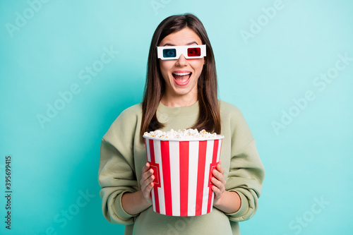 Photo portrait of cheerful screaming woman in 3d glasses holding big popcorn bucket isolated on vivid teal colored background