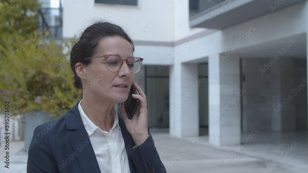 Serious businesswoman in office suit talking on mobile phone while standing outside. Static shot, copy space. Business communication concept. Serious businesswoman in office suit talking on mobile phone while standing outside. Static shot, copy space. Business communication concept.