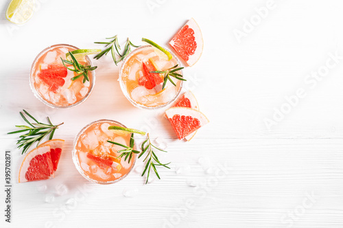 Paloma alcoholic cocktails with tequila and ice, garnished with lime wedges, grapefruit and rosemary stand on a white wooden table. Horizontal orientation, flat lay, copy space.