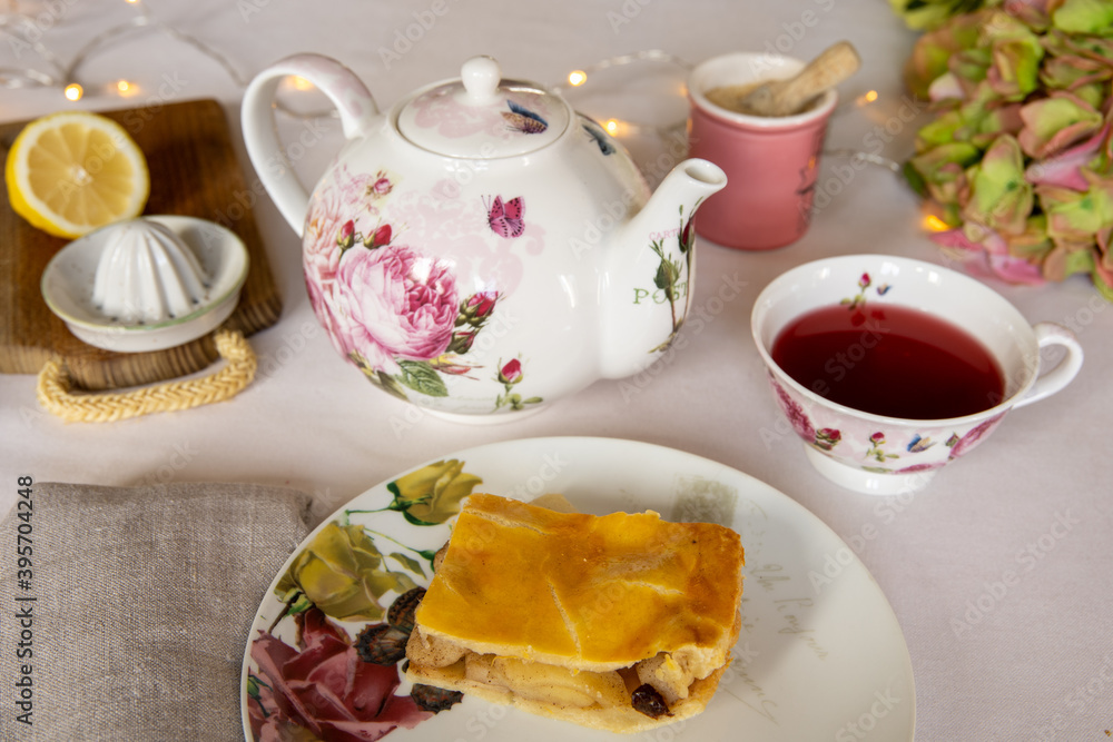 Teatime! Cute porcelain teapot and teacup and a piece of decked apple pie, on an elegant table with white table cloth. Teatime! Cute porcelain teapot and teacup and a piece of decked apple pie, on an elegant table with white table cloth.