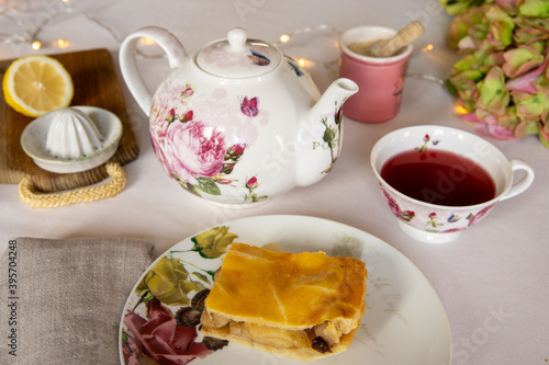 Teatime! Cute porcelain teapot and teacup and a piece of decked apple pie, on an elegant table with white table cloth.