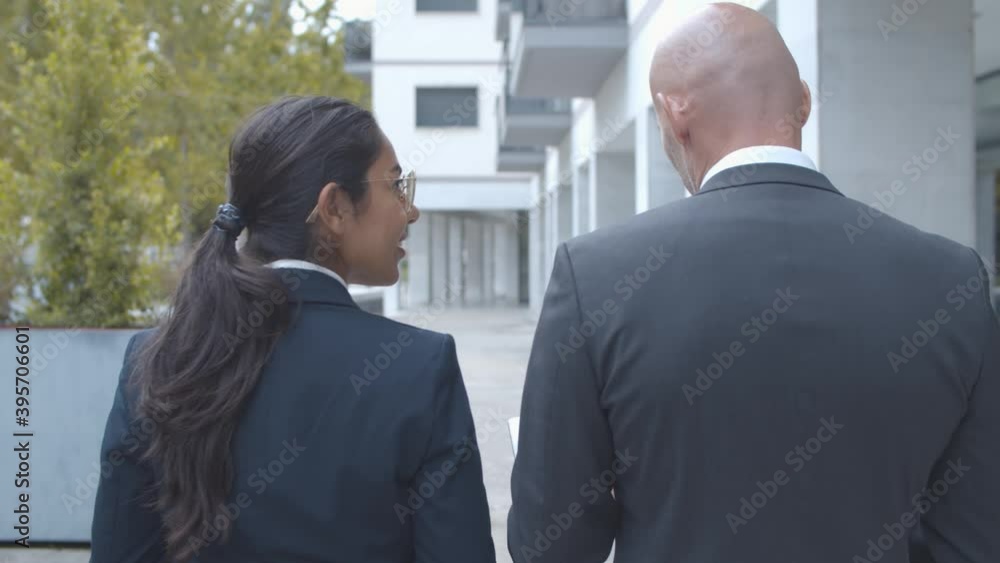Two managers discussing project and watching presentation on tablet while walking at office building outside. Back view, dolly shot. Business communication concept. Two managers discussing project and watching presentation on tablet while walking at office building outside. Back view, dolly shot. Business communication concept.