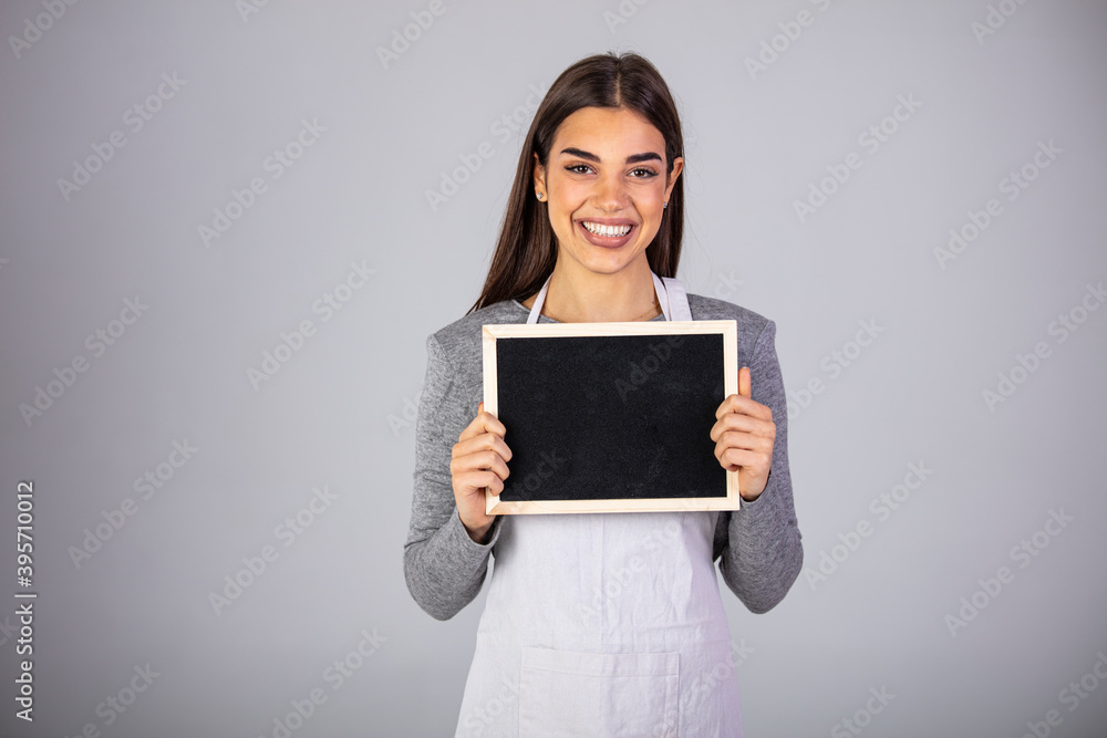 Beautiful Caucasian woman in barista apron holding empty blackboard sign studio shot - ready to insert text. Friendly smiling shop assistant holding blank chalkboard Beautiful Caucasian woman in barista apron holding empty blackboard sign studio shot - ready to insert text. Friendly smiling shop assistant holding blank chalkboard