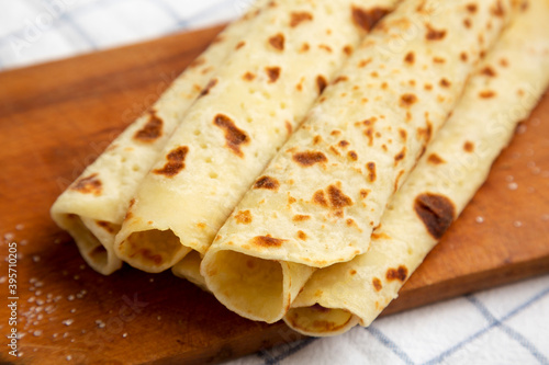 Homemade Norwegian Potato Flatbread (Lefse) with Butter and Sugar on a rustic wooden board on cloth, side view. Close-up. © Liudmyla