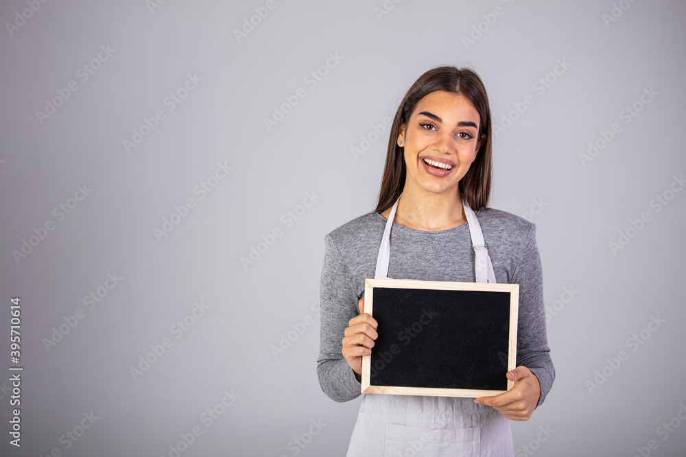 Beautiful Caucasian woman in barista apron holding empty blackboard sign studio shot - ready to insert text. Friendly smiling shop assistant holding blank chalkboard Beautiful Caucasian woman in barista apron holding empty blackboard sign studio shot - ready to insert text. Friendly smiling shop assistant holding blank chalkboard