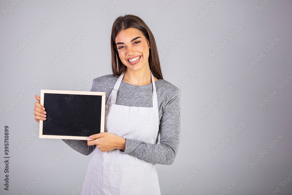 Beautiful Caucasian woman in barista apron holding empty blackboard sign studio shot - ready to insert text. Friendly smiling shop assistant holding blank chalkboard Beautiful Caucasian woman in barista apron holding empty blackboard sign studio shot - ready to insert text. Friendly smiling shop assistant holding blank chalkboard