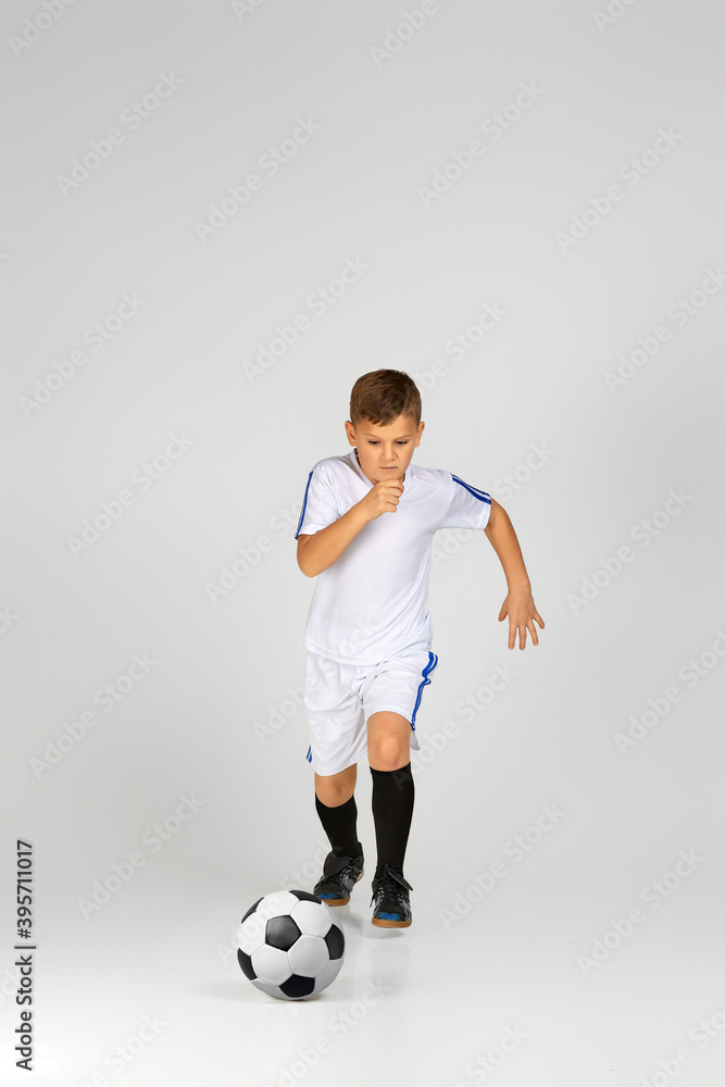 little child boy in uniform playing with soccer ball over studio background.
