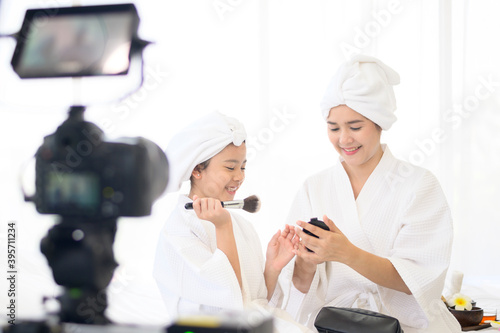 Video camera filming happy mom and daughter in white bathrobe acting for movie, behind the scenes of shoot
